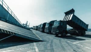 Commercial trucks at a port terminal beside a roll-on roll-off vessel ramp, commercial truck shipping
